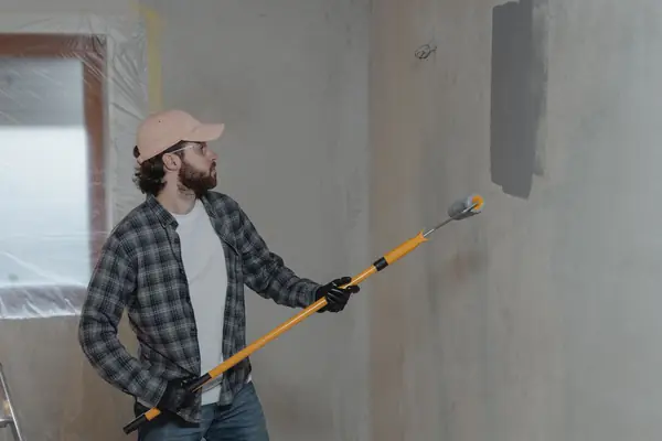 Painter rolling grey paint onto an interior wall in Toledo